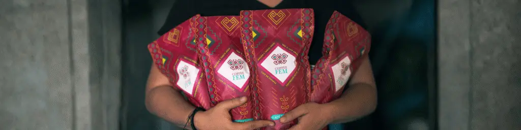 Persona sostiene varios paquetes de Coffee FEM, café producido por mujeres organizadas que impulsan su autonomía económica mediante el comercio de productos con valor agregado.