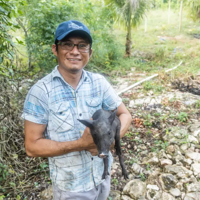Productor rural sostiene un lechón negro en brazos mientras sonríe, como parte de un proyecto de producción pecuaria familiar.