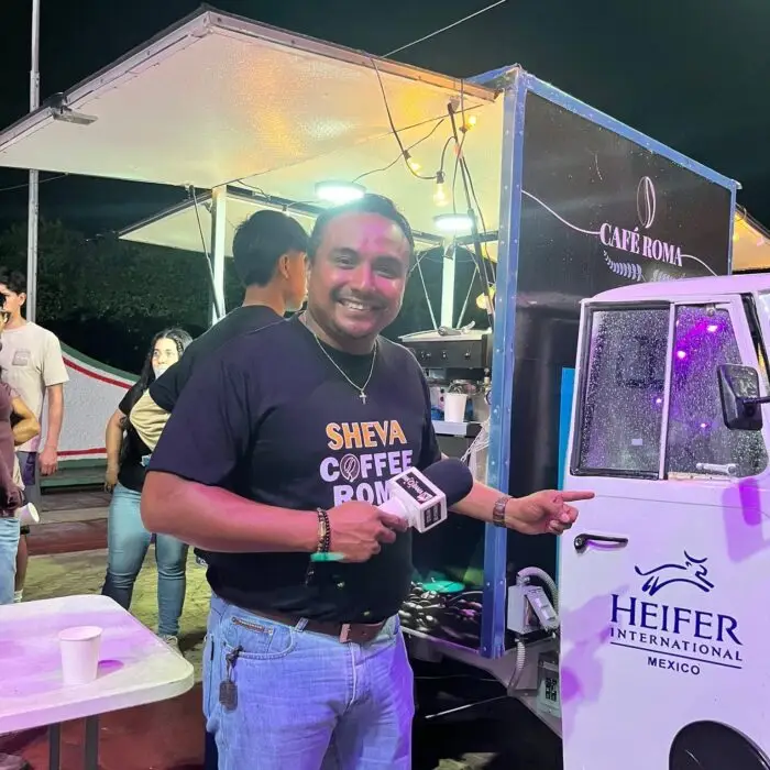 Representante de un emprendimiento de café ofrece una entrevista frente a una motocafetería de Heifer México durante un evento nocturno.