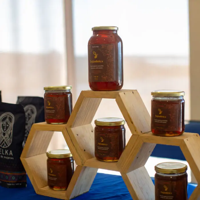 Exhibición de frascos de miel Enjámbrica sobre una estructura de madera en forma de panal, acompañados de productos de café local.