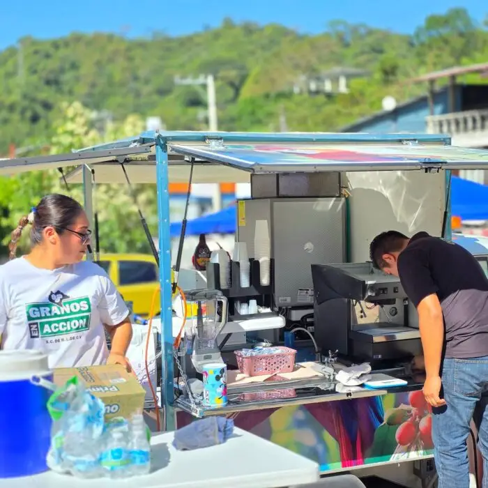 Equipo de Granos en Acción prepara bebidas en una motocafetería equipada con máquina de espresso durante una jornada de atención al público.