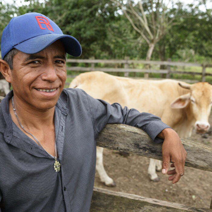 Productor ganadero apoyado sobre un corral con ganado al fondo, reflejando el manejo responsable de los animales en una unidad de producción.