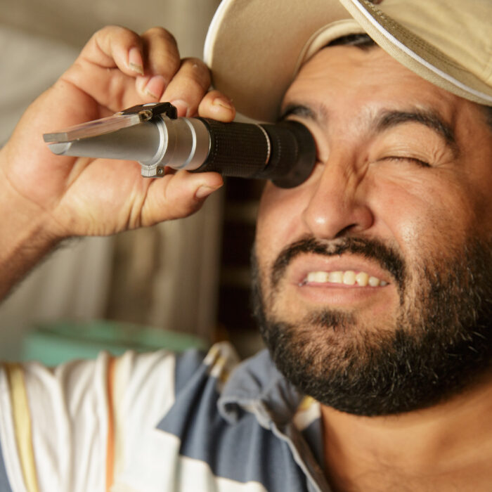 Productor rural utilizando un refractómetro portátil para medir la calidad o concentración de una muestra agrícola.
